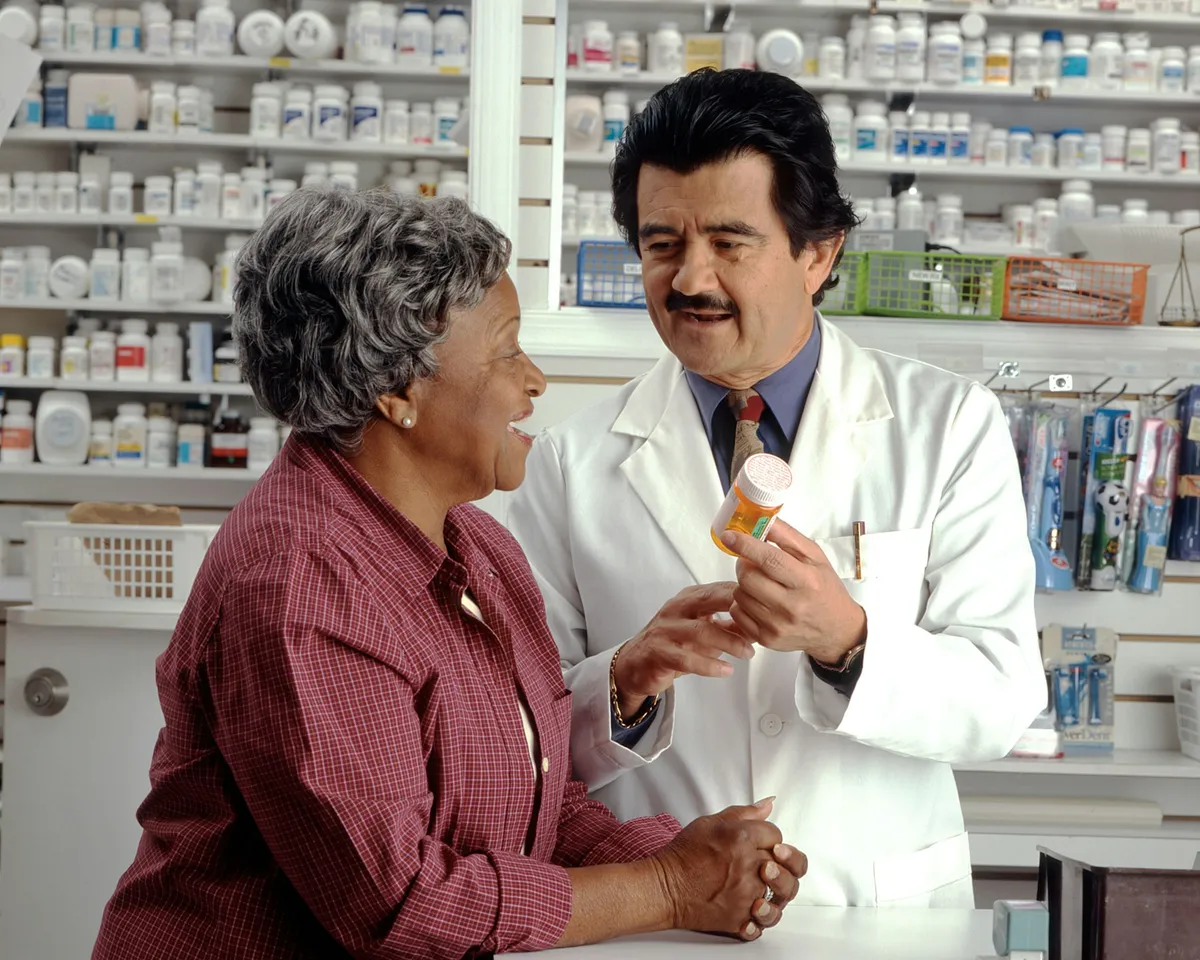 A pharmacist explaining a prescription bottle to an older patient at the counter