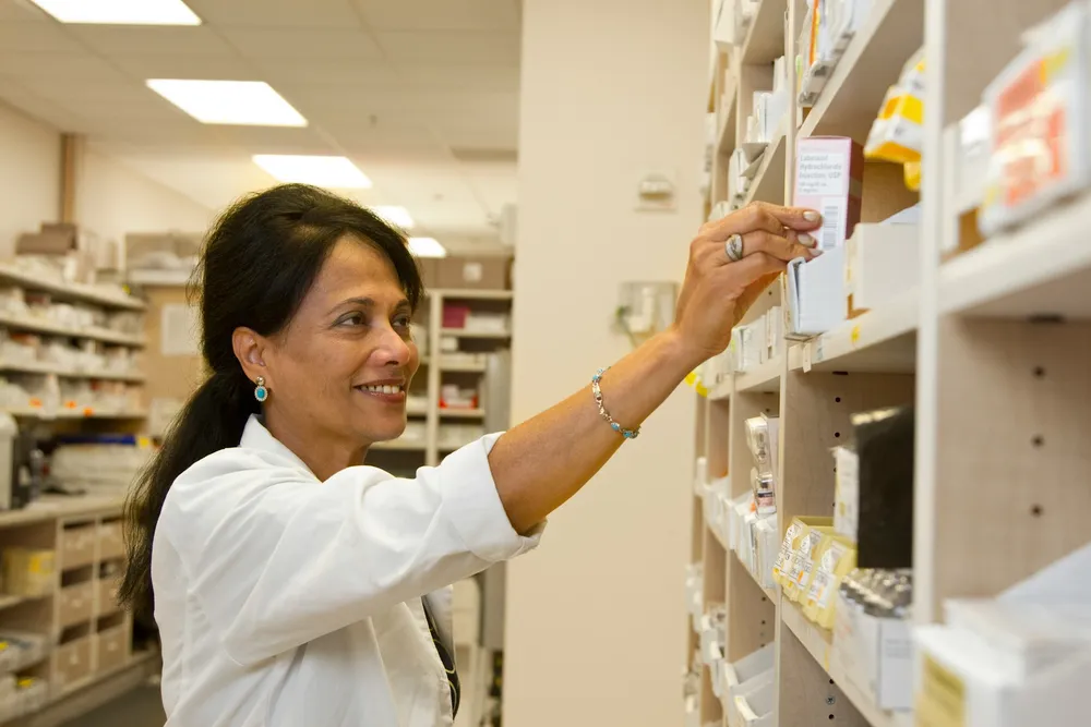 A pharmacist reaching for a medication box on a pharmacy shelf